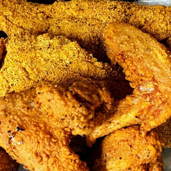 Crispy golden fried chicken pieces and fish fillets in a black takeout container.