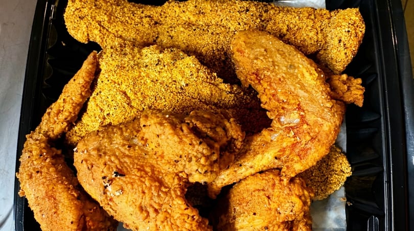 Crispy golden fried chicken pieces and fish fillets in a black takeout container.